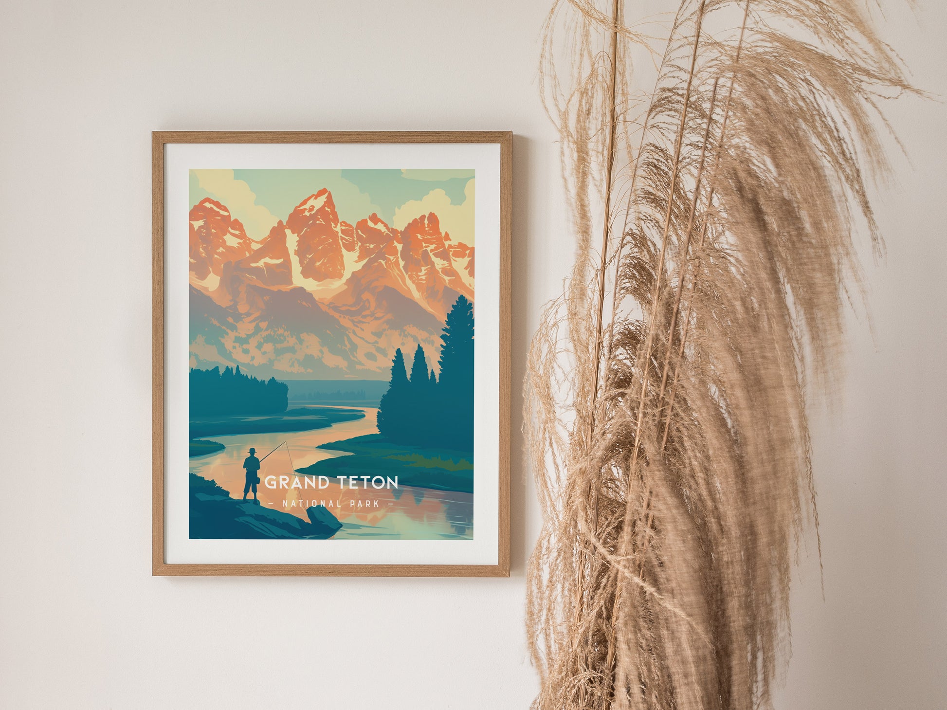 Framed Grand Teton National Park poster features a minimalist design with mountains, a river, and a fisherman. Tall, dried grasses are visible to the right of the artwork.