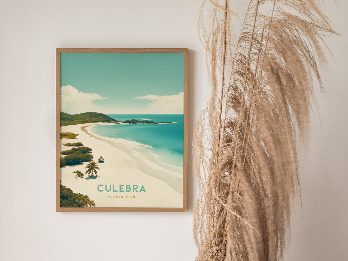 Framed poster of Culebra, Puerto Rico beach with turquoise waters and lush greenery, displayed beside tall, dried pampas grass against a light wall.