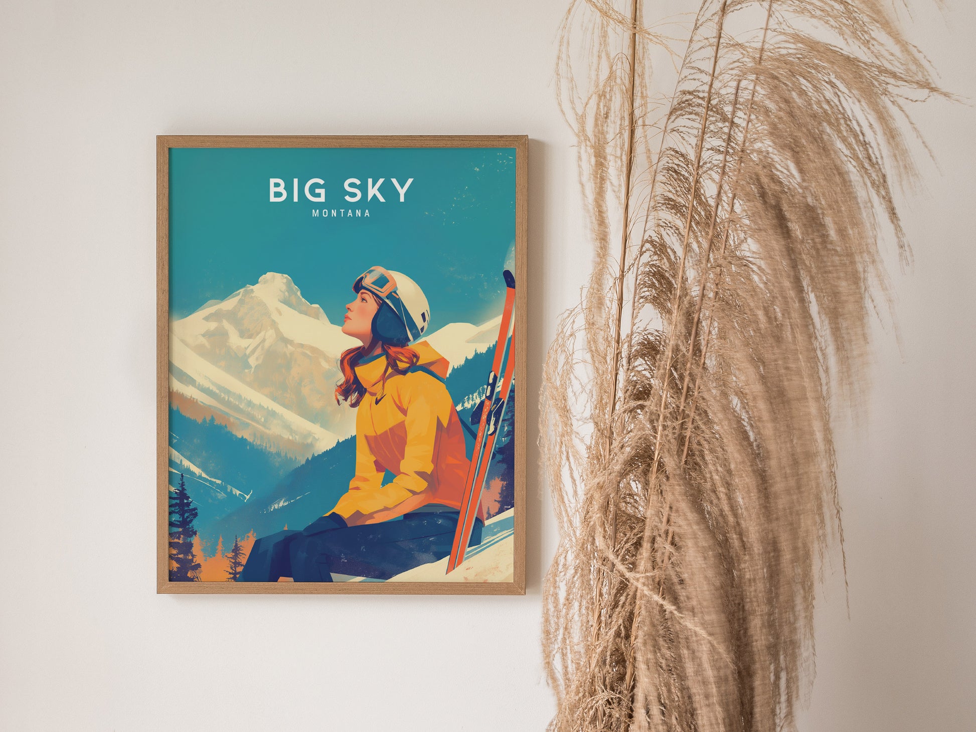 A framed poster titled Big Sky Montana shows a woman in a yellow jacket and helmet gazing at a snowy mountain peak, with pampas grass nearby.
