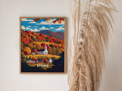 A framed poster depicting a white church steeple amidst vibrant autumn foliage in Stowe, Vermont, is displayed on a wall next to decorative pampas grass.
