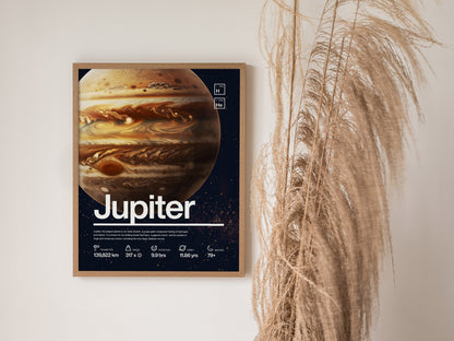 A framed Jupiter poster with bold equatorial bands and the Great Red Spot is displayed on a wall beside tall, dried grasses.