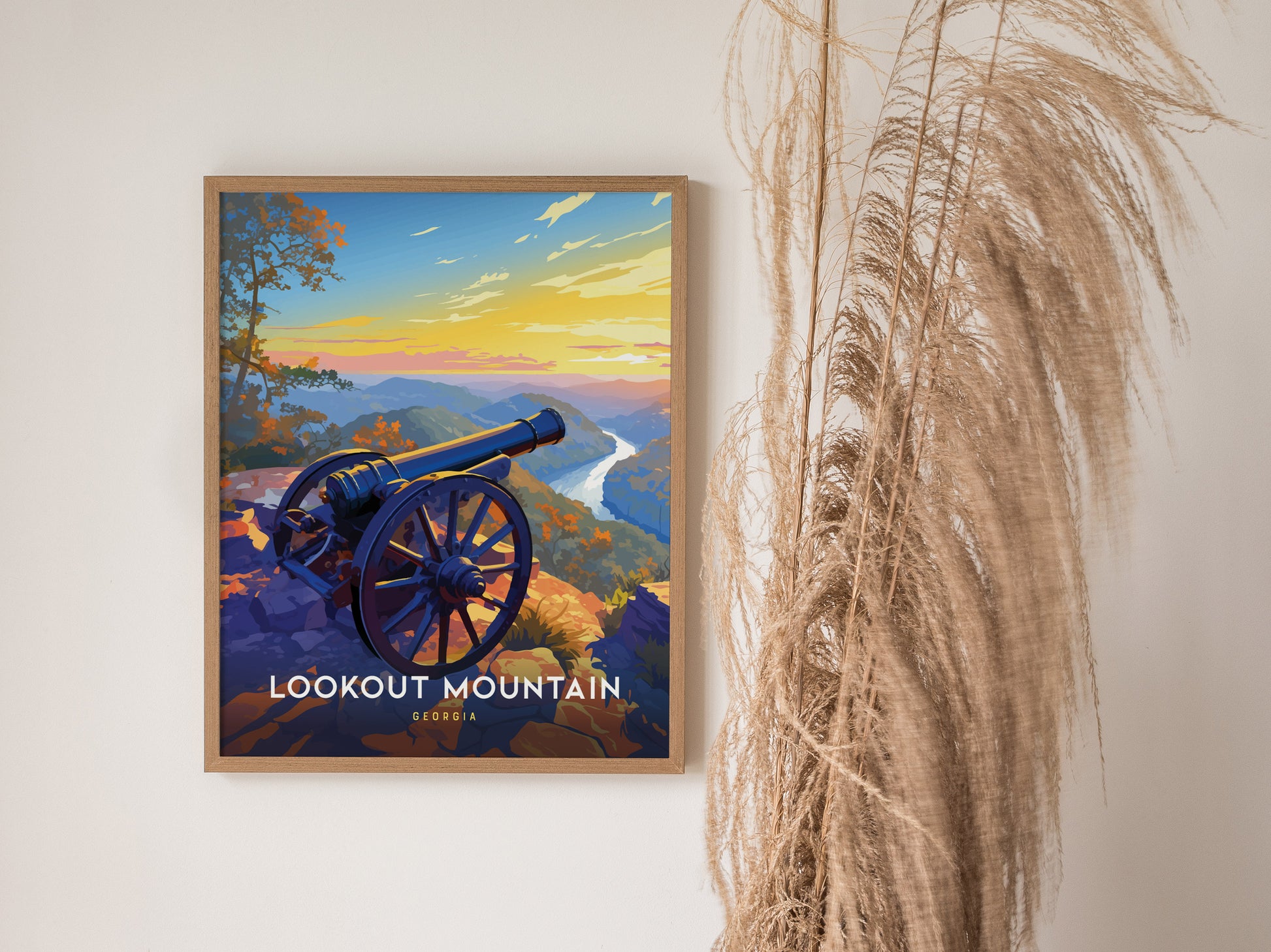 A framed poster of Lookout Mountain, Georgia, featuring a cannon overlooking a scenic sunset landscape, is displayed on a wall beside decorative dried grasses.