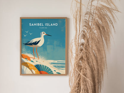A framed poster of Sanibel Island features an illustrated sandpiper on a beach with seashells. Decorative grasses are placed beside the artwork, enhancing the coastal theme.