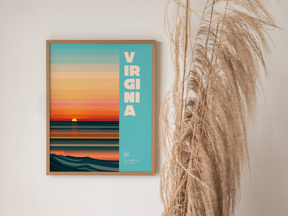 A framed poster with a stylized sunset over the ocean and the word Virginia on a blue background, alongside tall dried grasses.