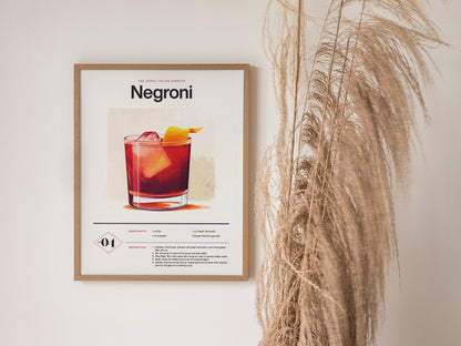 Framed Negroni cocktail poster featuring a vibrant drink illustration and recipe, with decorative dried grasses beside it against a plain wall.