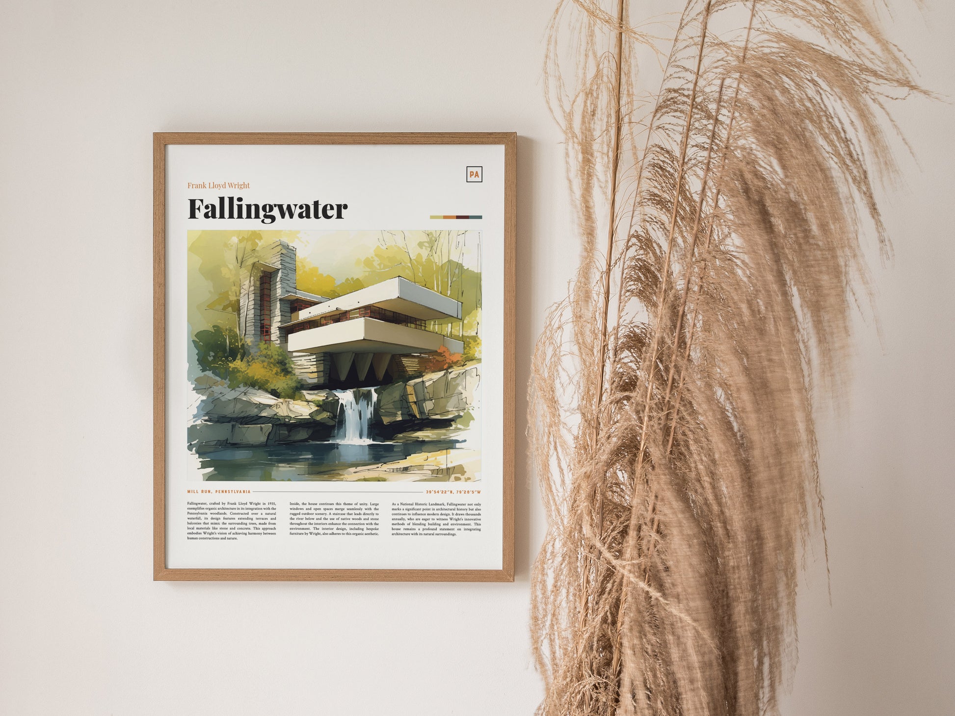 A framed Fallingwater poster featuring a watercolor illustration of the iconic architecture hangs on a wall next to tall, dried pampas grass.
