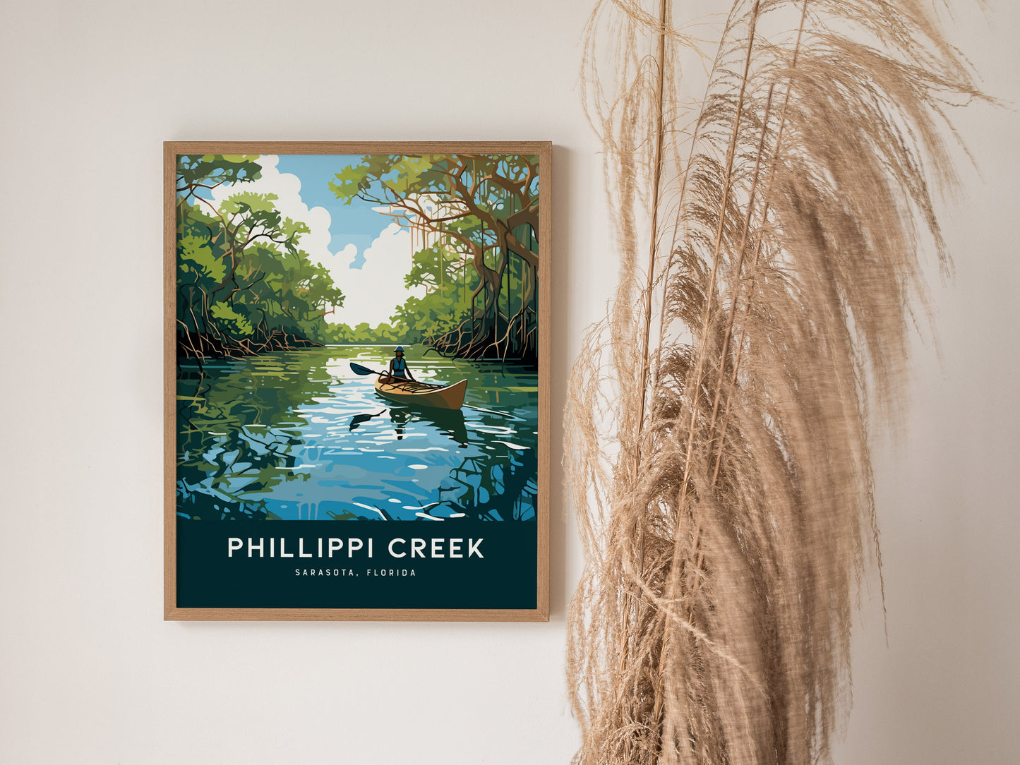 A framed poster depicts a kayaker on a tranquil creek surrounded by lush mangroves under a blue sky. The text reads Phillippi Creek, Sarasota, Florida.