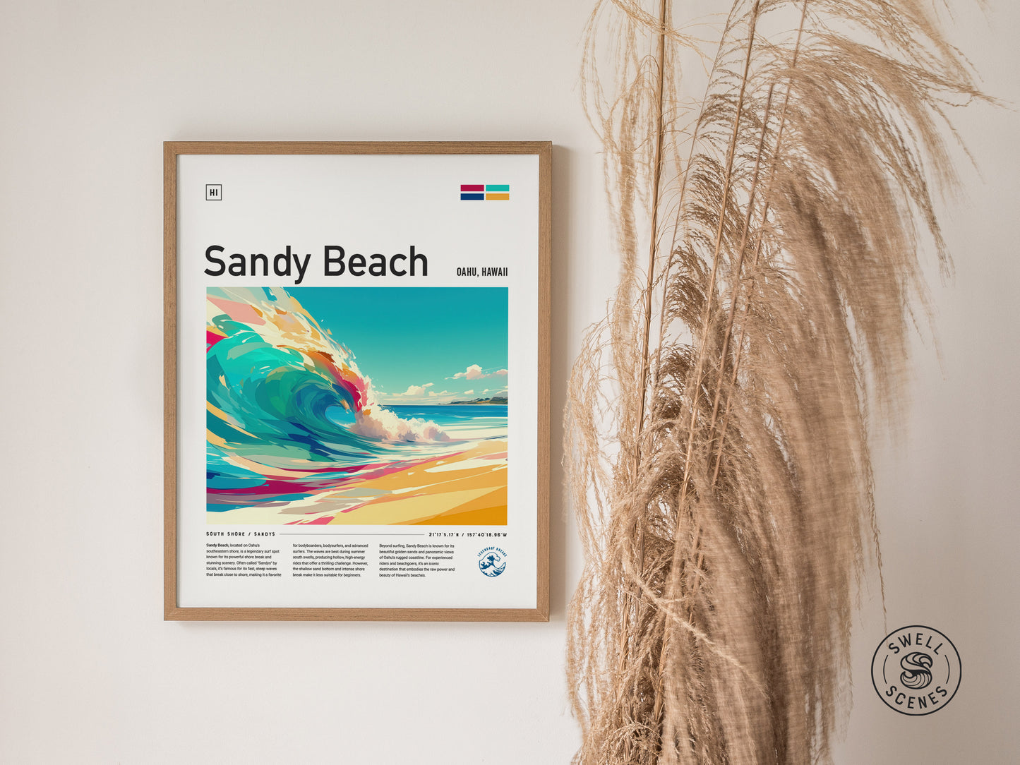 Framed Sandy Beach poster featuring vibrant, stylized waves and text, displayed on a wall beside dried pampas grass. The Swell Scenes logo is visible in the lower right corner.