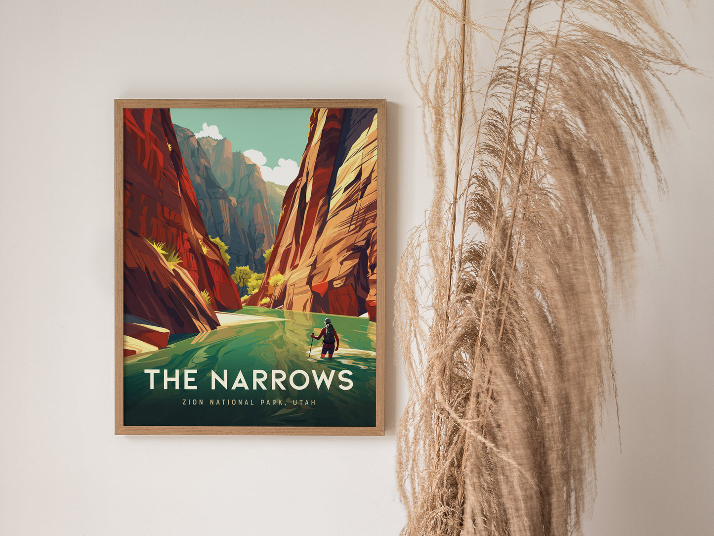 Framed poster of The Narrows at Zion National Park, depicting vibrant slot canyons and a hiker by the river. Decorative pampas grass is visible beside the artwork.