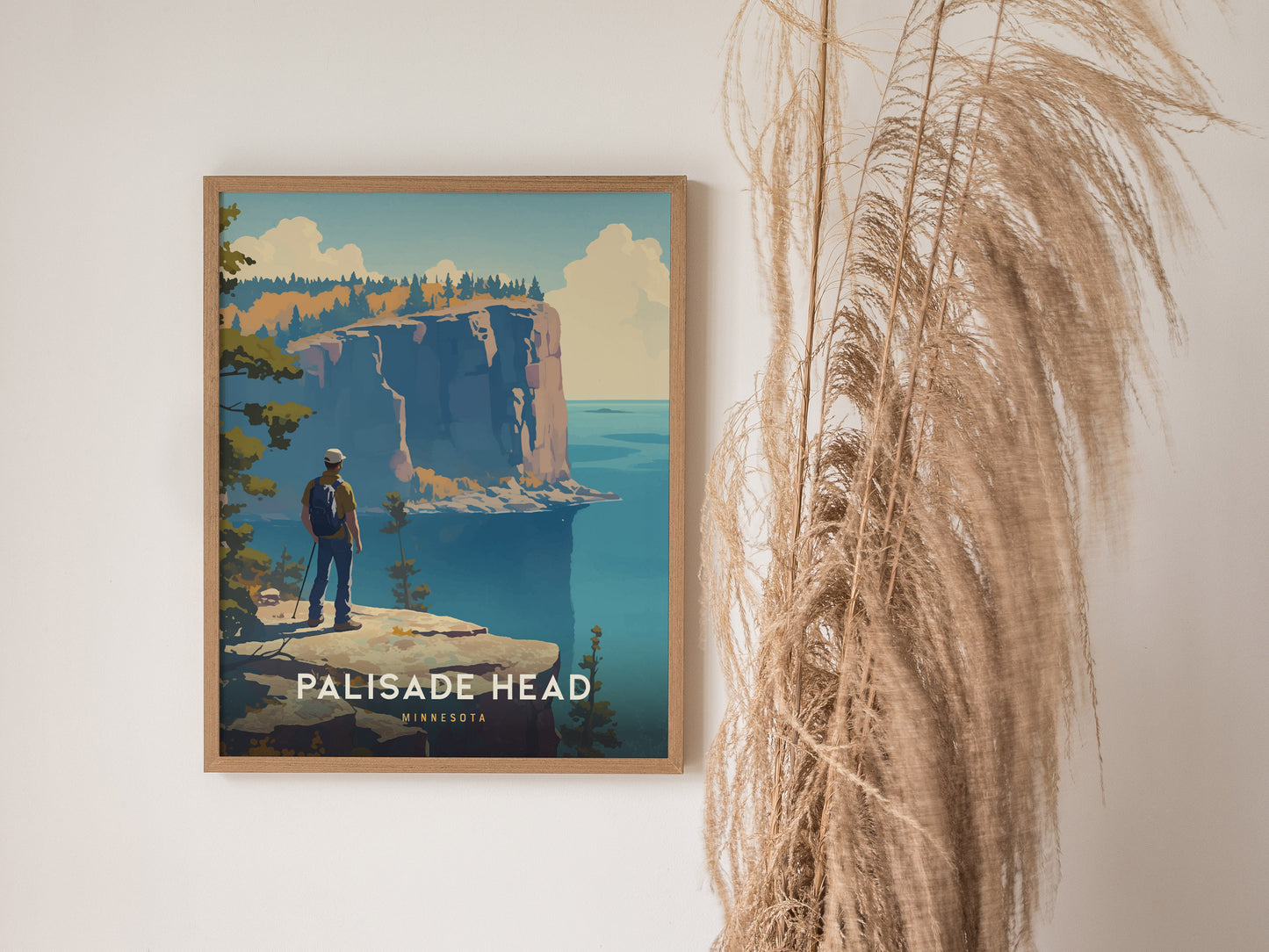 A framed poster of Palisade Head in Minnesota features a hiker overlooking dramatic cliffs and Lake Superior, with pampas grass decor beside it.