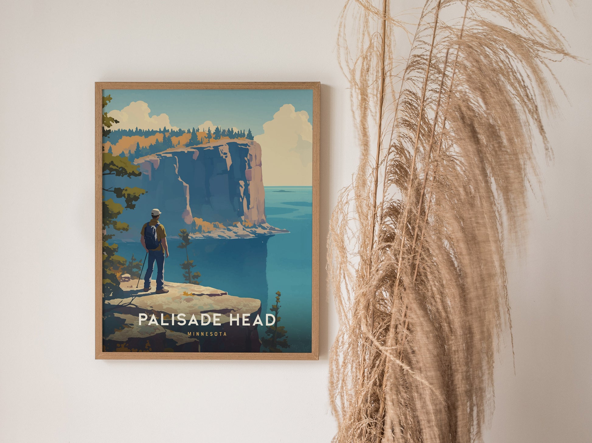 A framed poster of Palisade Head in Minnesota features a hiker overlooking dramatic cliffs and Lake Superior, with pampas grass decor beside it.