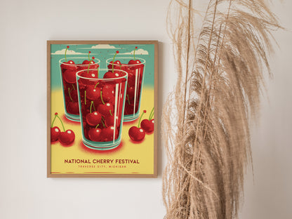 A framed poster on a wall features three glasses filled with cherries and the text National Cherry Festival, Traverse City, Michigan. Pampas grass decorates the right side.