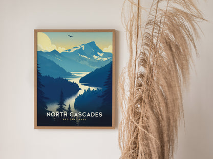 A framed poster of North Cascades National Park featuring stylized mountains, a winding lake, and a soaring bird, displayed next to tall, dried pampas grass.