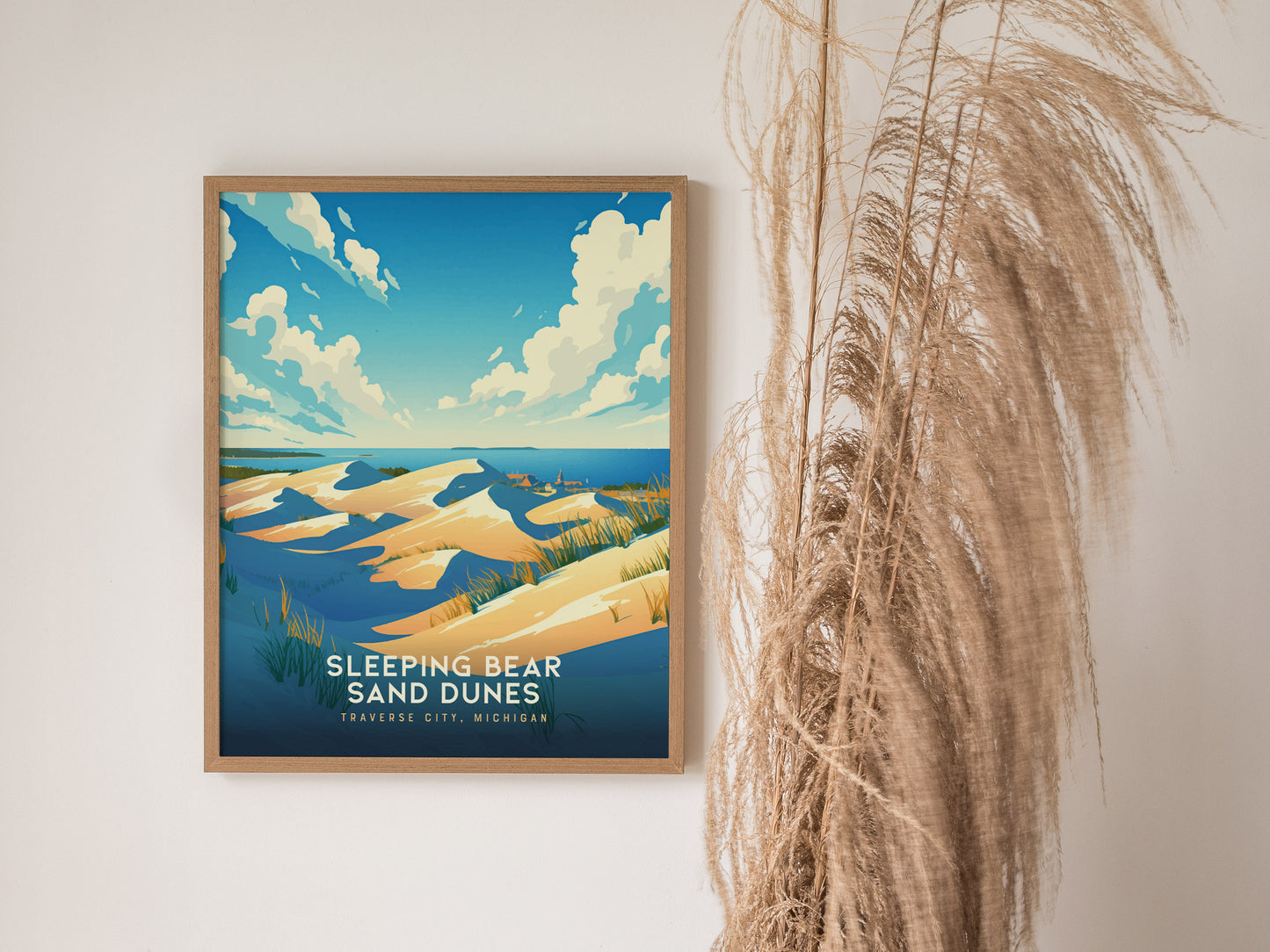 Framed Sleeping Bear Sand Dunes poster featuring golden sand dunes and blue skies, displayed next to dried pampas grass against a white wall.