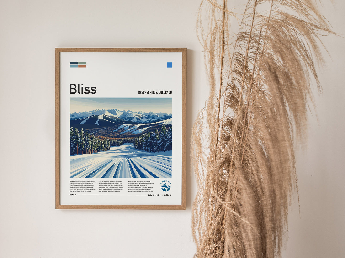 A framed poster titled Bliss features a snowy landscape with mountains and evergreens, displayed on a wall beside tall, dried grass.