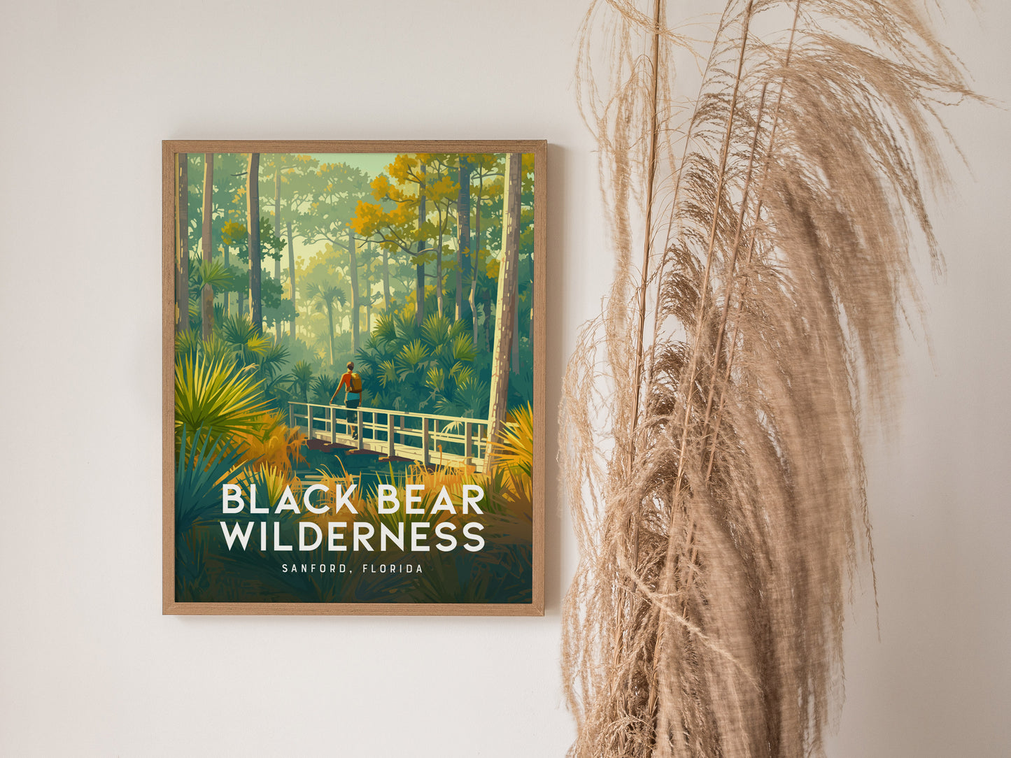 A framed poster titled Black Bear Wilderness shows a hiker on a bridge surrounded by lush greenery and tall trees, with pampas grass nearby.