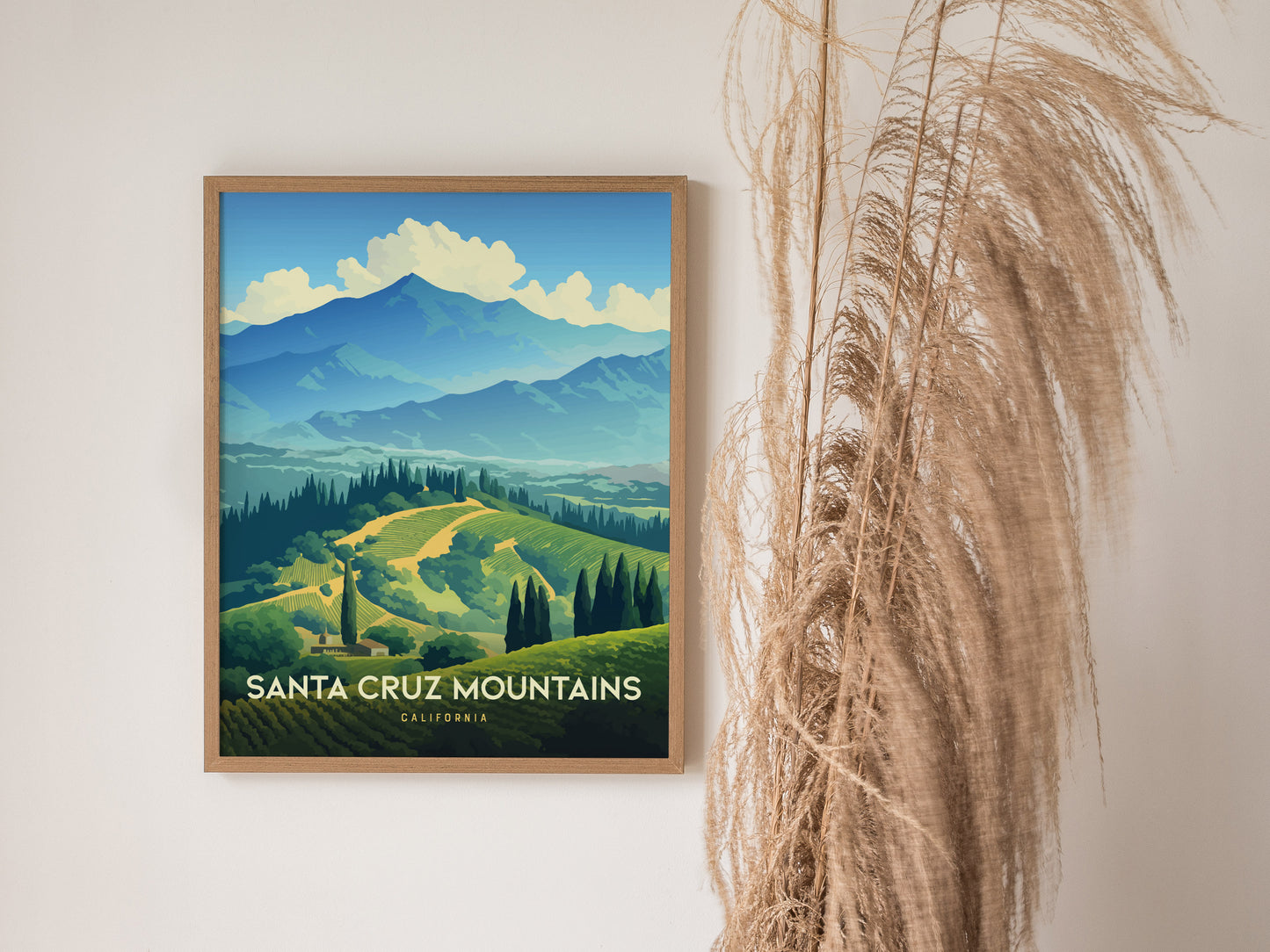 A framed poster of the Santa Cruz Mountains, featuring rolling green hills and a blue mountain backdrop, hangs on a wall next to decorative dried grass.