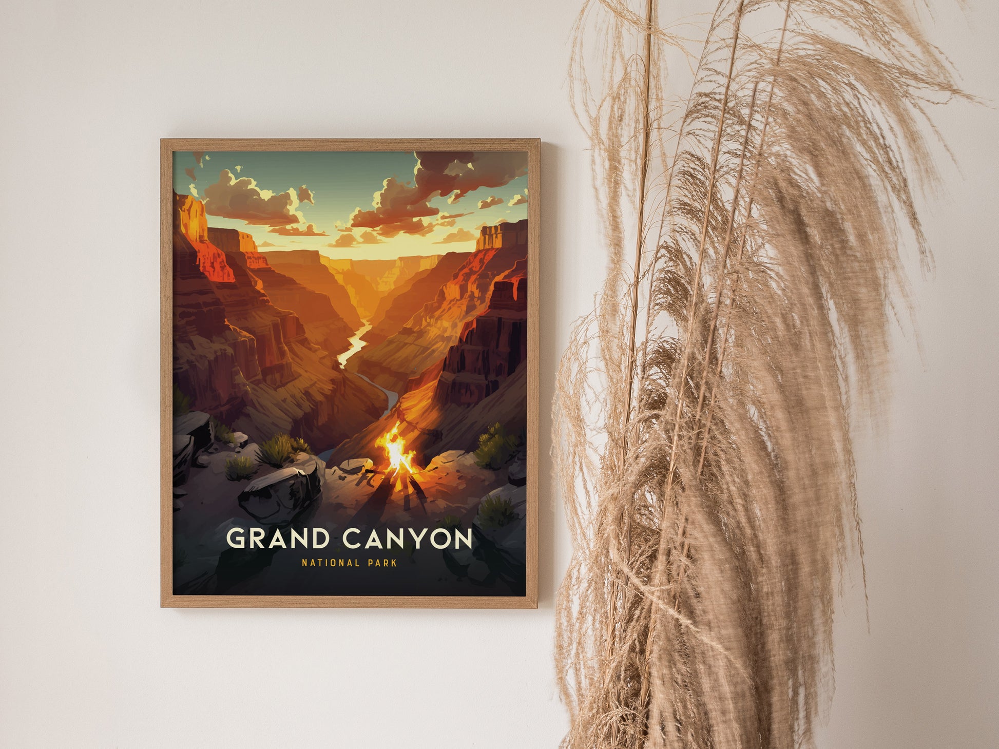 A framed Grand Canyon poster hangs on a white wall, depicting a vibrant sunset over the canyon with a small campfire. Tall, dry grass decorates the right side.