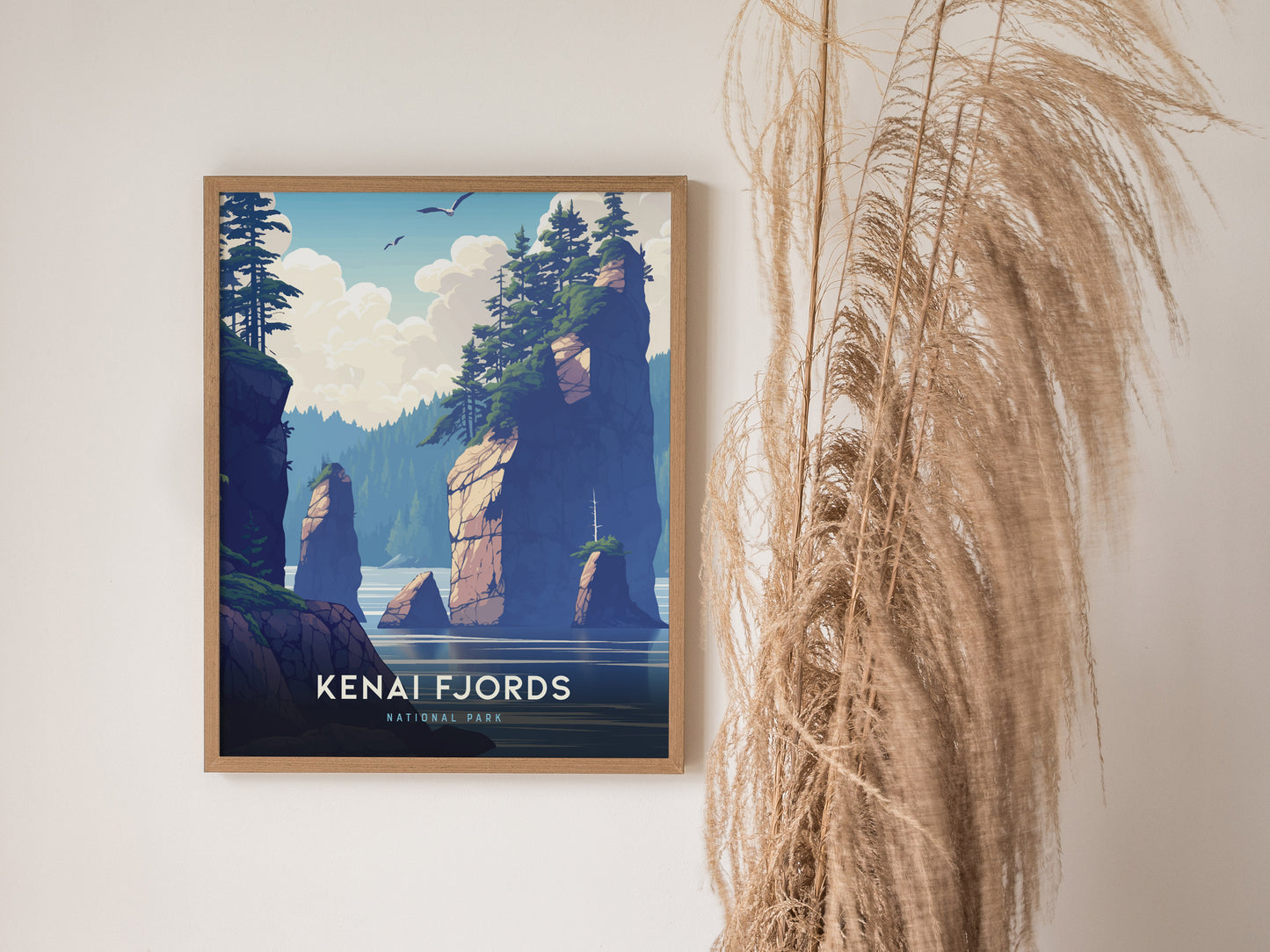 A framed poster of Kenai Fjords National Park features illustrated cliffs and trees, with seagulls flying above. Its displayed on a wall alongside tall, dried grass.