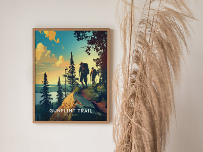 A framed poster titled Gunflint Trail depicts hikers on a scenic ridge surrounded by pine trees, with a dramatic sunset sky. Tall, dried grasses are positioned beside the artwork.