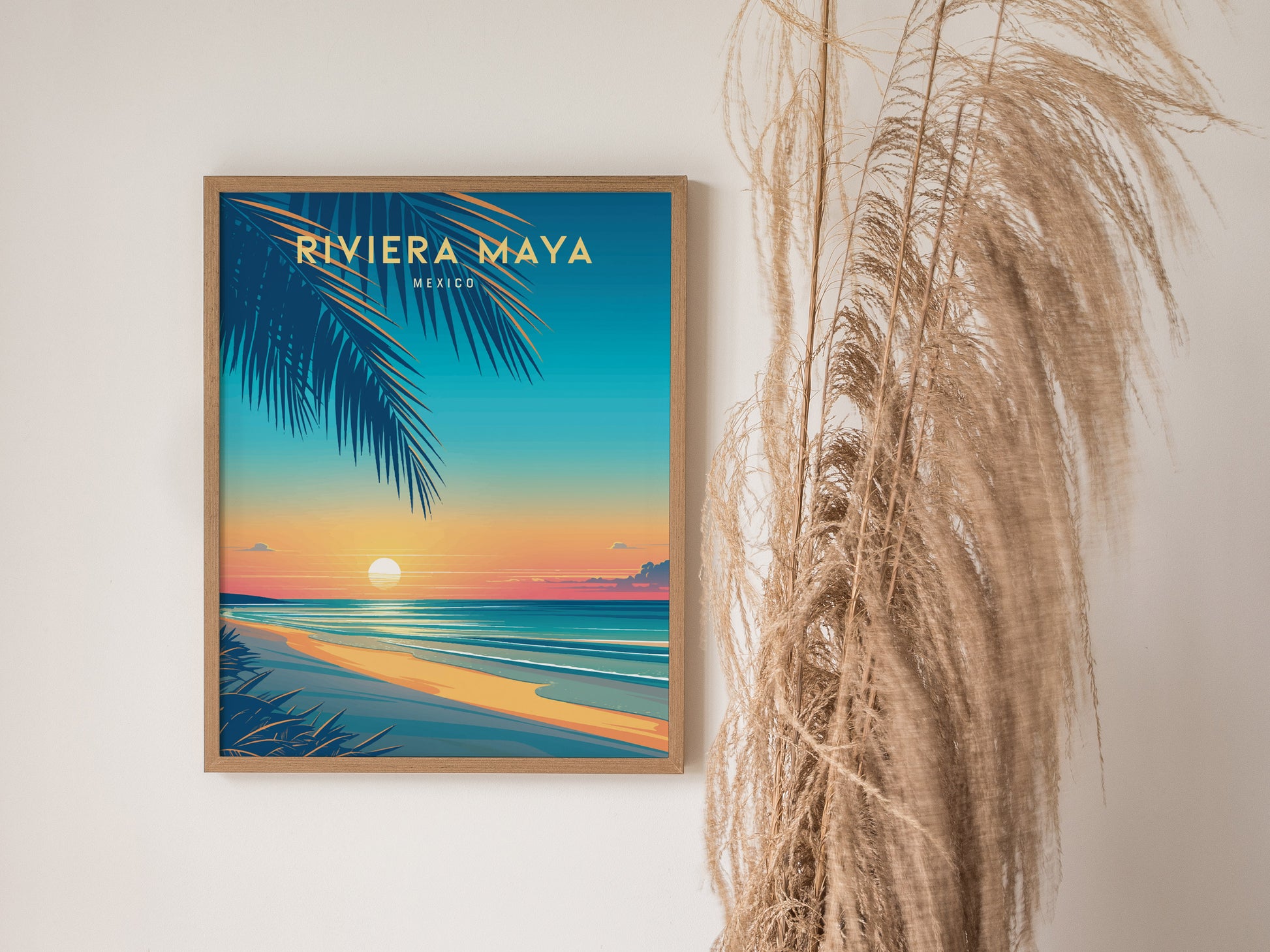 A framed Riviera Maya travel poster features a vibrant beach scene with a sunset over turquoise waters and palm leaves. Dried pampas grass decorates the adjacent wall.