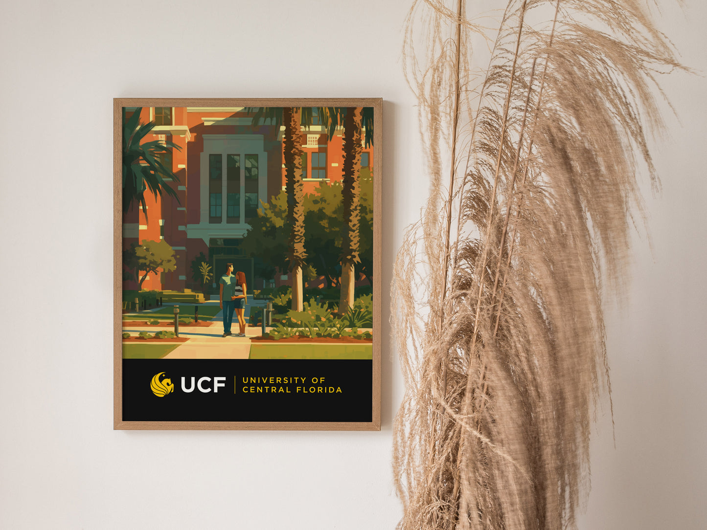 A framed University of Central Florida poster on a wall depicts two people walking on a campus pathway surrounded by palm trees and modern architecture.