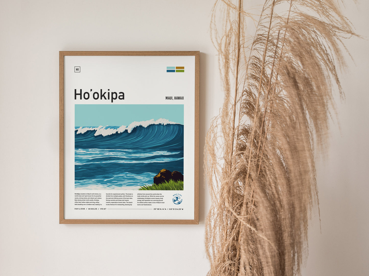 A framed poster of Hookipa Beach, featuring an illustrated ocean wave, hangs on a white wall next to dried pampas grass. The poster includes text about Maui, Hawaii.
