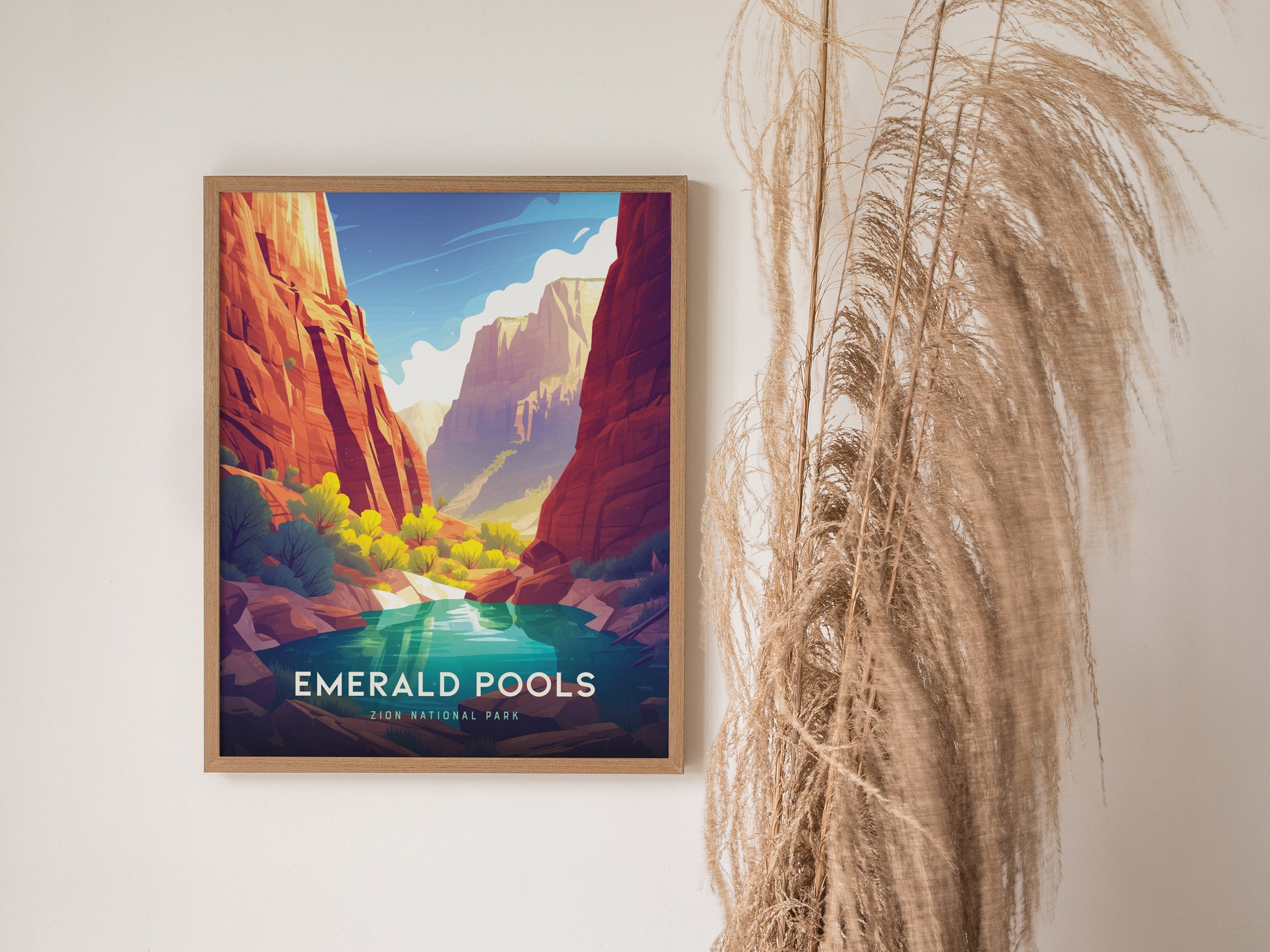 Framed poster of Zion National Parks Emerald Pools, featuring vibrant canyon cliffs and a serene turquoise pool, hangs on a wall beside tall, dried ornamental grass.