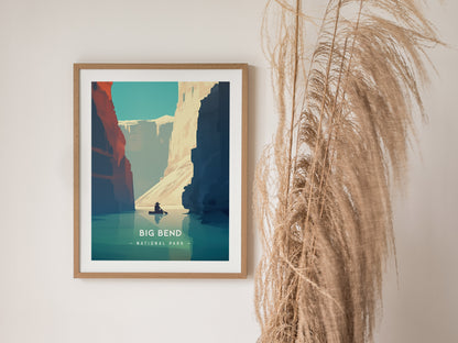 Framed Big Bend National Park poster featuring minimalist artwork of the Rio Grande canyon with a person kayaking. Tall dried grass decorates the wall beside the artwork.