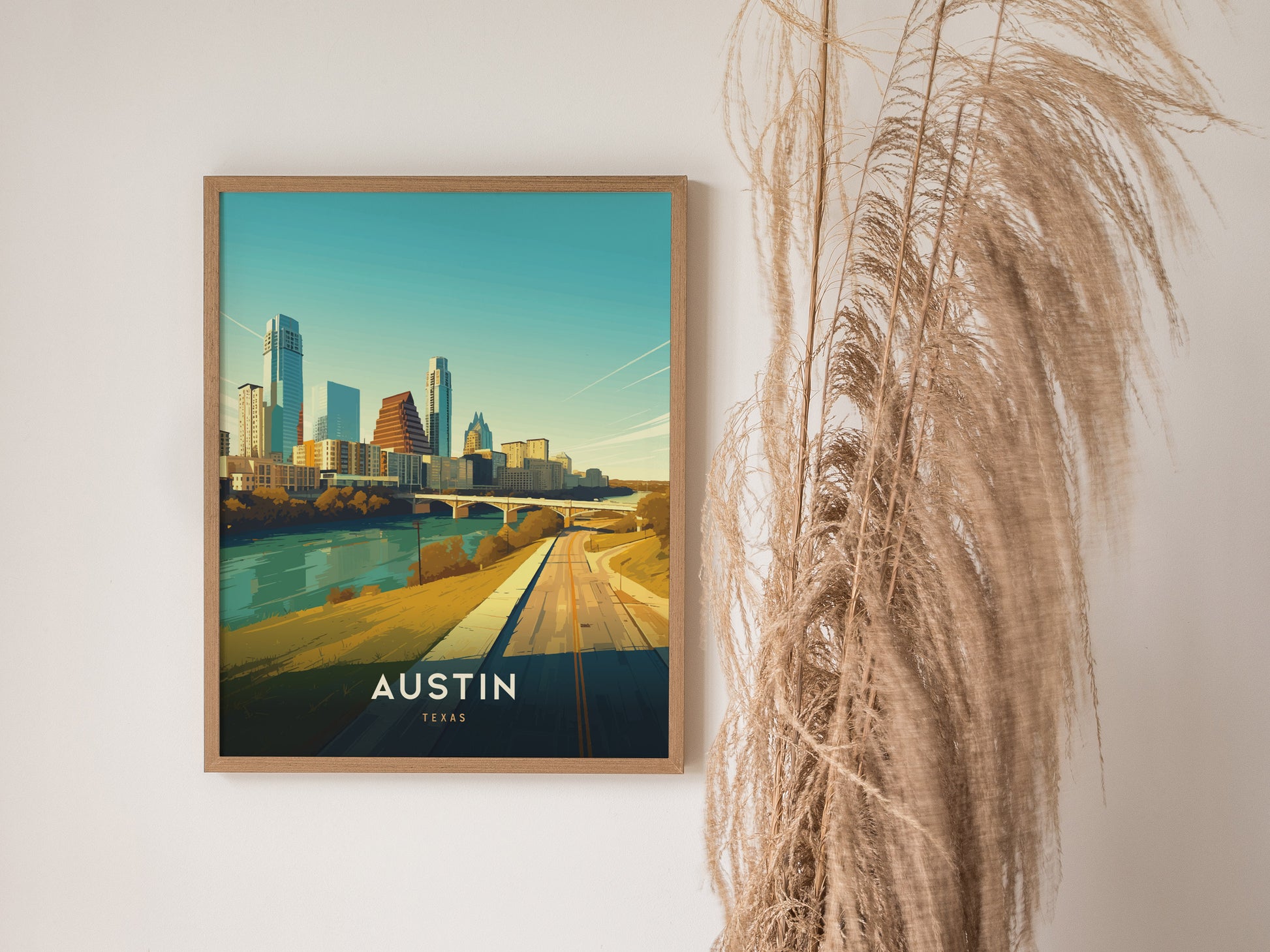 Framed poster of the Austin, Texas skyline with modern buildings and a river, displayed on a wall next to tall, dried grasses.