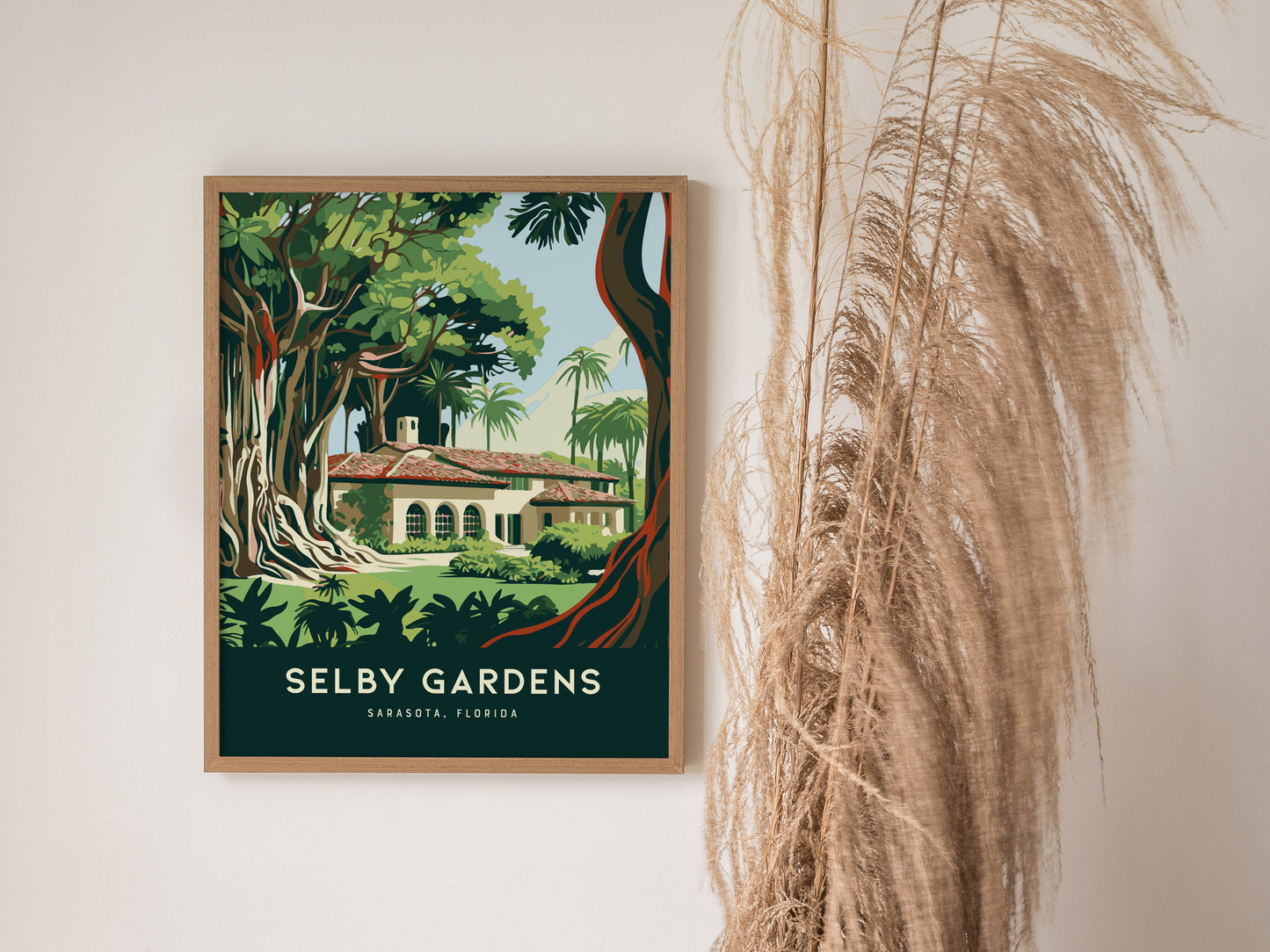 A framed poster titled Selby Gardens showcases lush tropical trees and a building, set against a white wall beside dried pampas grass.