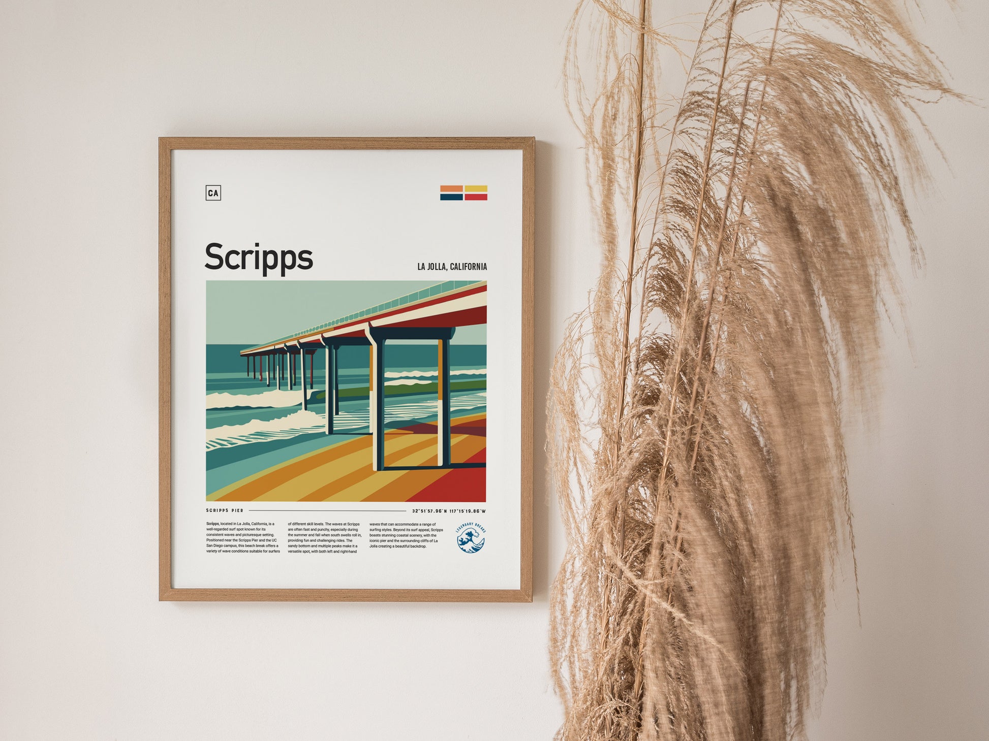 Framed poster of Scripps Pier in La Jolla, California, featuring bold lines and vibrant colors, hangs on a wall beside tall, dried ornamental grasses.