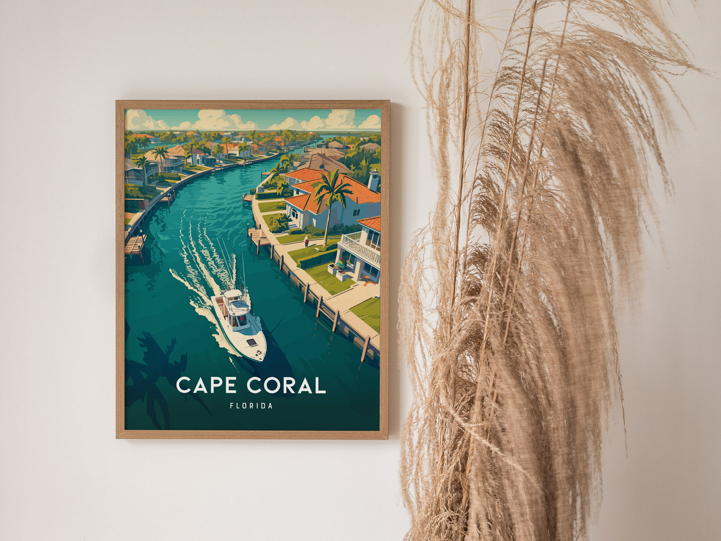 A framed poster of Cape Coral, Florida, depicts a boat on a canal lined with tropical homes and palm trees. Tall dried grasses are positioned beside the artwork.