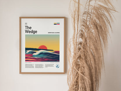 A framed poster titled The Wedge depicts stylized waves and a vibrant sunset at Newport Beach, California. It hangs on a wall next to tall, wispy dried grasses.
