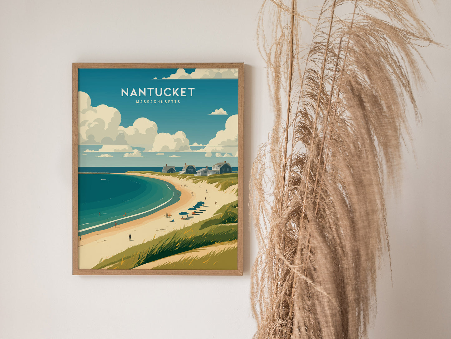 A framed Nantucket Massachusetts poster featuring a coastal scene with sandy beaches, ocean waves, and cottages under a cloudy sky, displayed beside dried pampas grass.