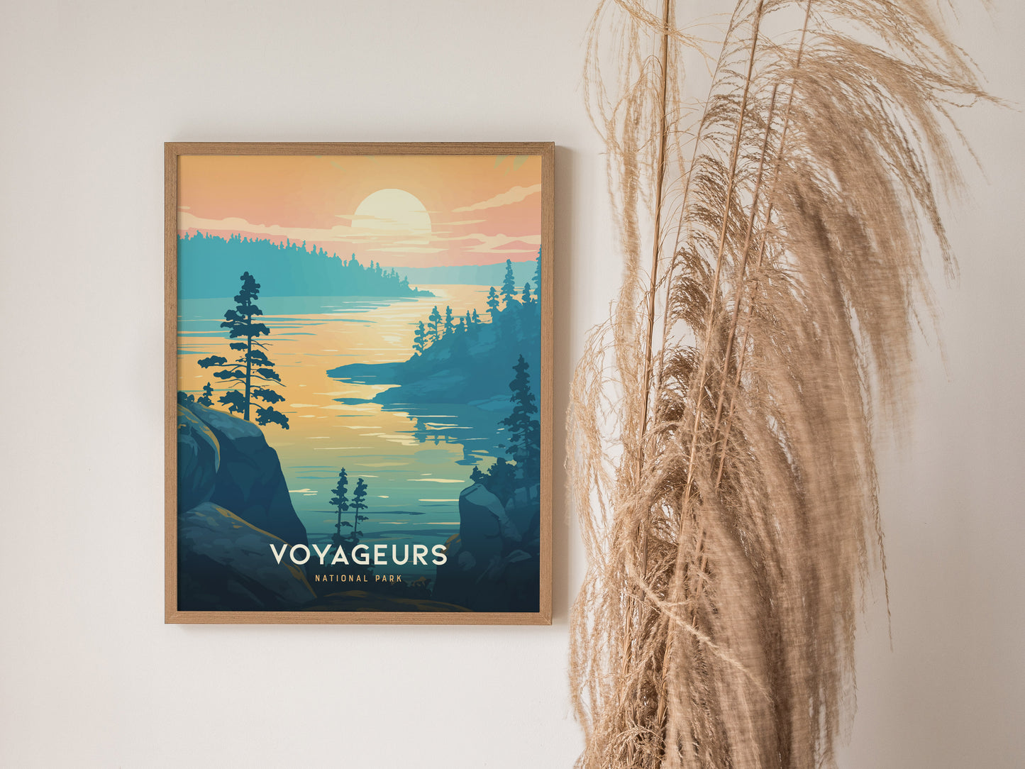 Framed artwork of Voyageurs National Park featuring a serene sunset over a lake, surrounded by pine trees and rocky cliffs. Tall dried plants are visible beside the artwork.