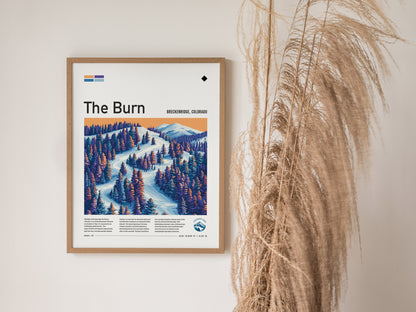 A framed poster titled The Burn depicts a colorful ski run with snow-covered trees and mountains, set against a warm gradient sky. Pampas grass decorates the right side.