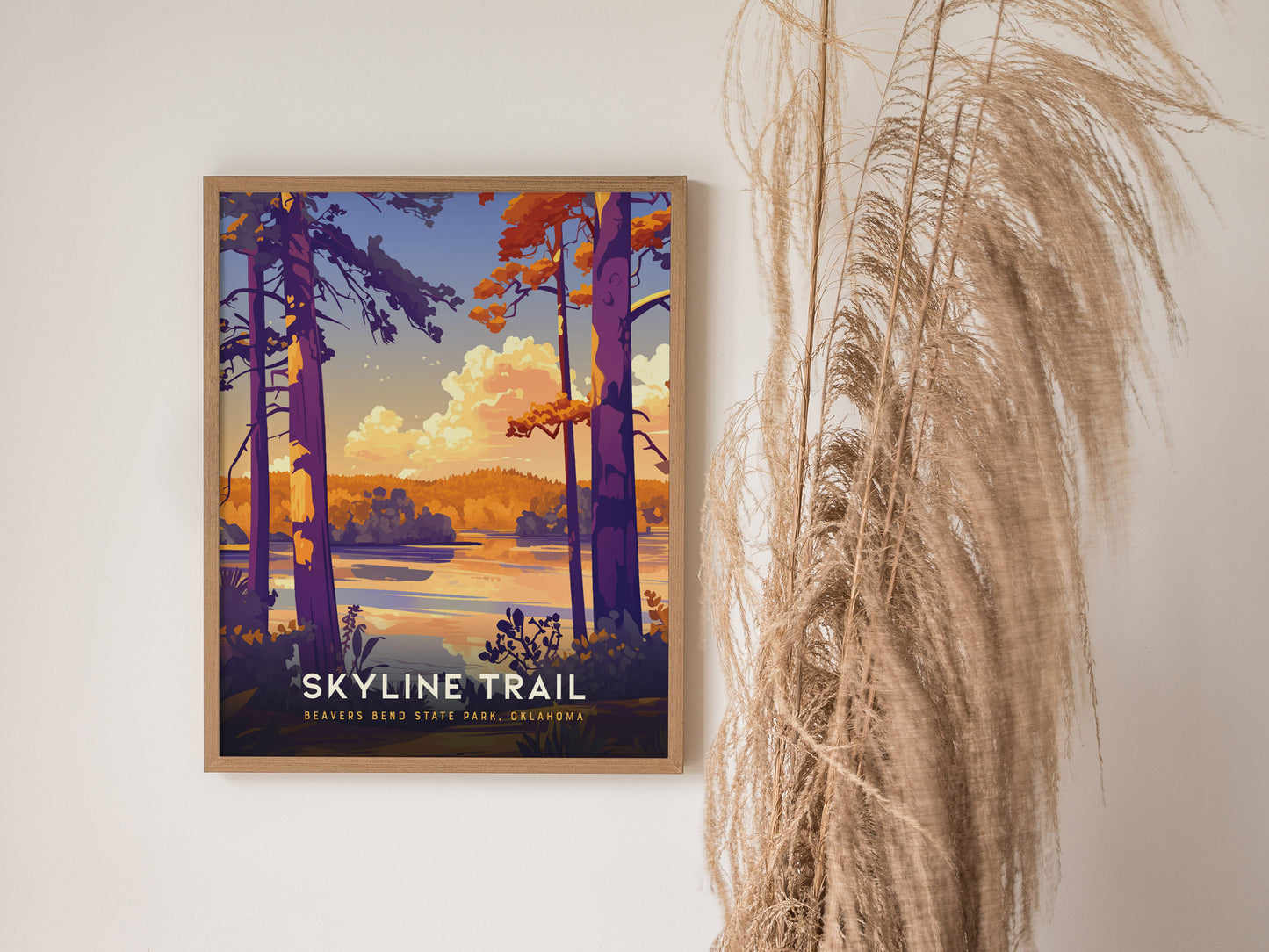 A framed artwork titled Skyline Trail depicts a vibrant landscape with tall trees, a serene lake, and colorful clouds. It is displayed next to dried pampas grass.