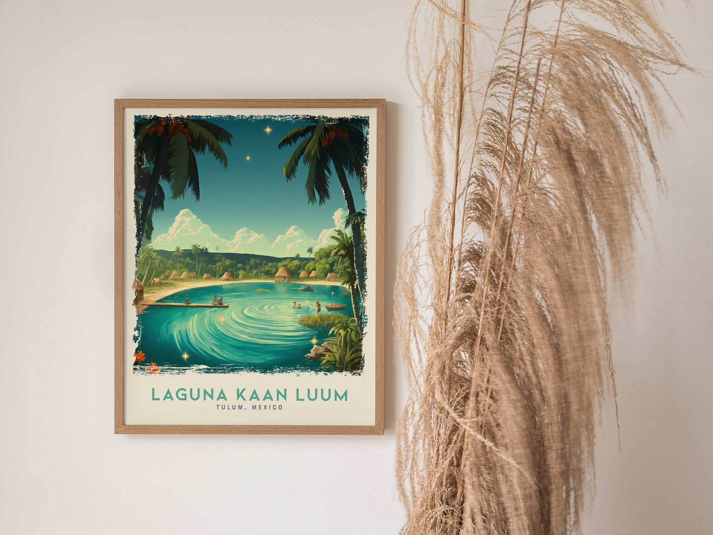 A framed poster of Laguna Kaan Luum features a turquoise lagoon surrounded by palm trees under a clear sky, with decorative pampas grass beside it.
