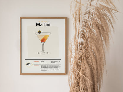 A framed martini cocktail poster featuring a classic dry martini illustration and recipe hangs on a wall beside tall, dried pampas grass.