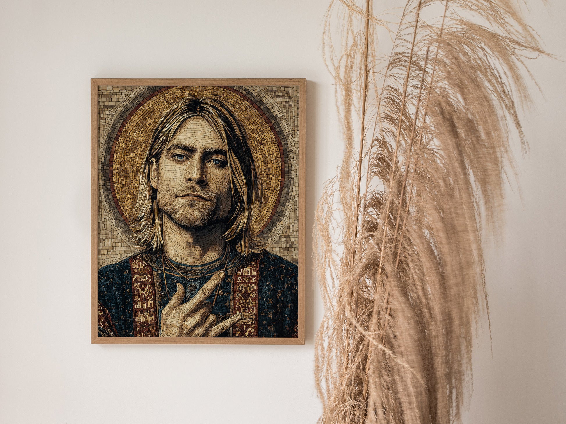 A framed mosaic artwork of a male figure with long hair, making a hand gesture, is displayed on a white wall. Dried pampas grass stands nearby.