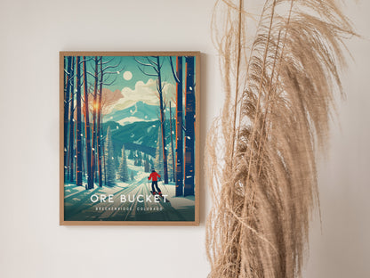 A framed poster of a winter forest scene with a skier, set against a mountain backdrop, hangs on a wall beside decorative dried grass.