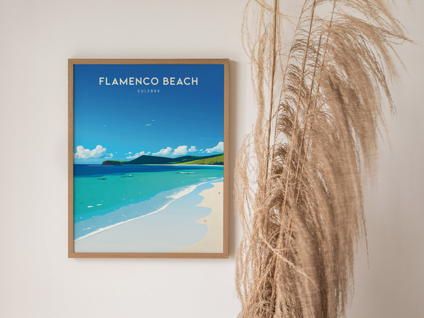 A framed poster of Flamenco Beach with turquoise waters and white sands hangs on a wall beside tall, dried pampas grass.