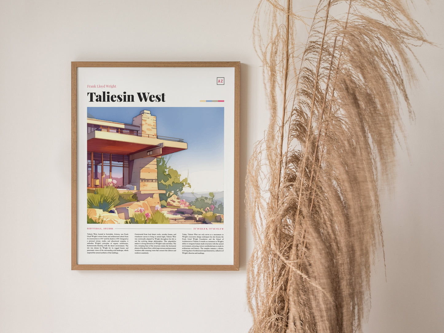 A framed Taliesin West poster by Frank Lloyd Wright hangs on a white wall, with tall, dried pampas grass displayed beside it.