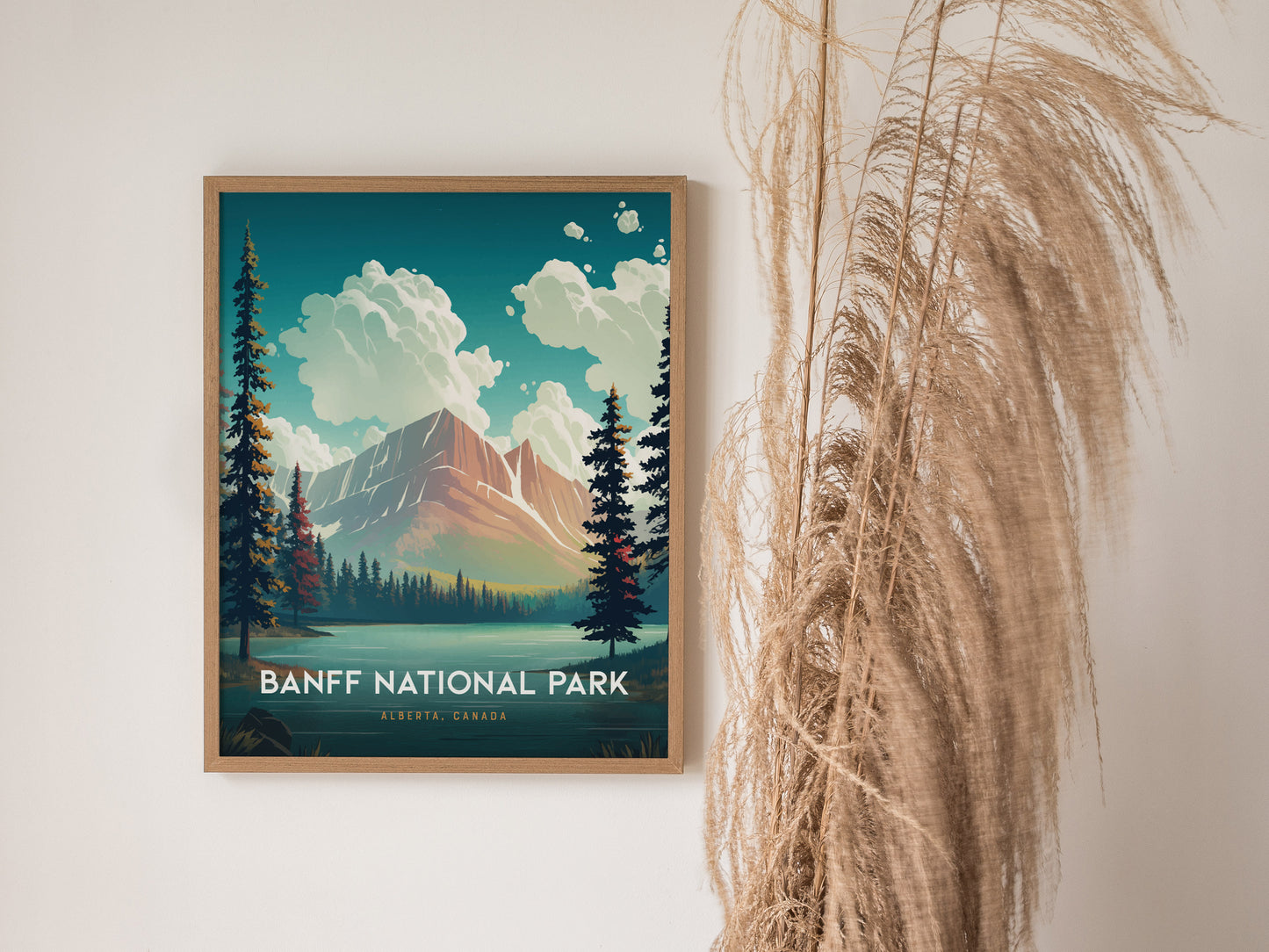 A framed Banff National Park poster features a mountain scene with turquoise waters and trees, displayed on a white wall beside decorative dried grasses.