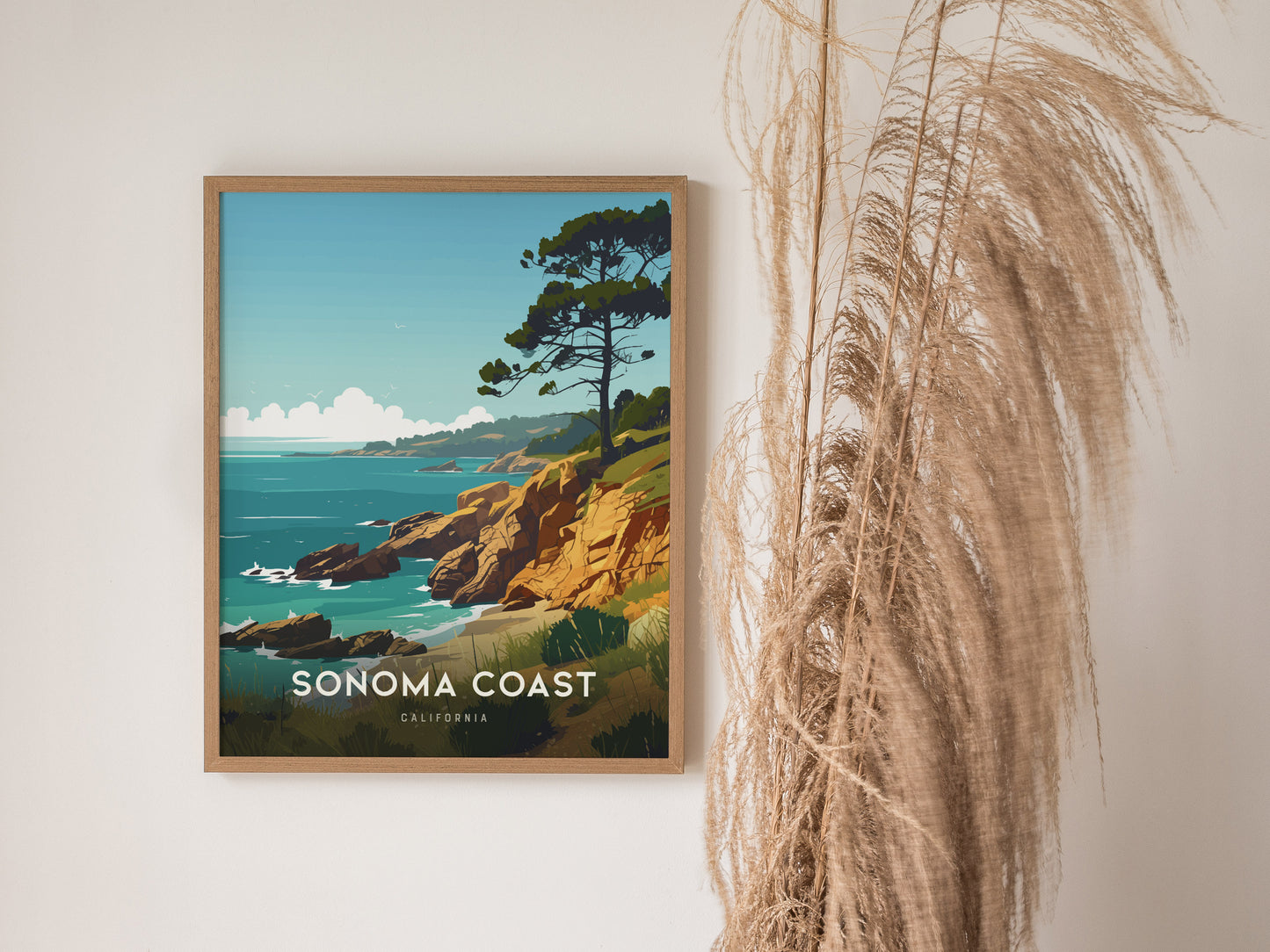 Framed Sonoma Coast poster featuring rocky cliffs and a tree overlooking the ocean, with decorative pampas grass beside it. The artwork captures a tranquil coastal scene.