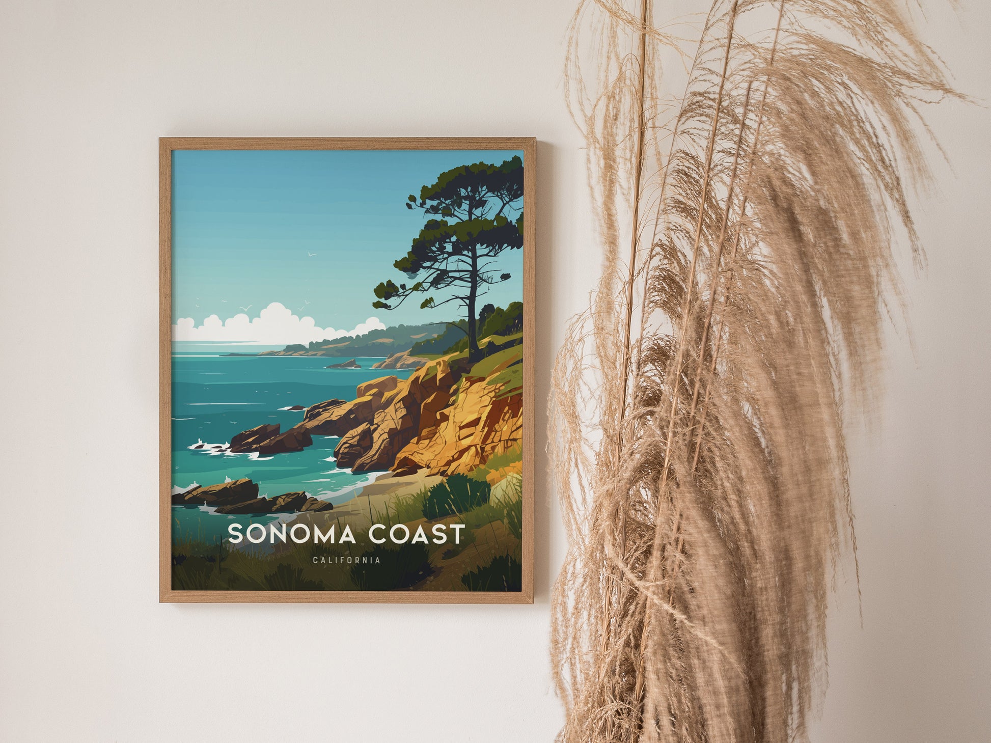 Framed Sonoma Coast poster featuring rocky cliffs and a tree overlooking the ocean, with decorative pampas grass beside it. The artwork captures a tranquil coastal scene.