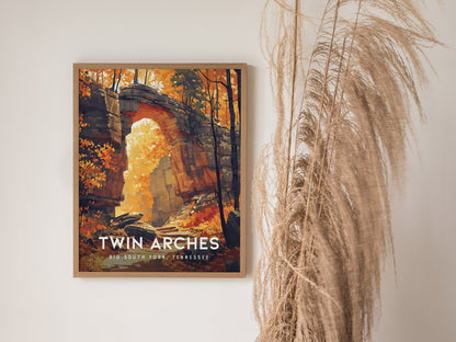 A framed poster of the Twin Arches in Big South Fork, Tennessee, features vibrant autumn foliage and sandstone formations. It is displayed next to decorative dried plants.