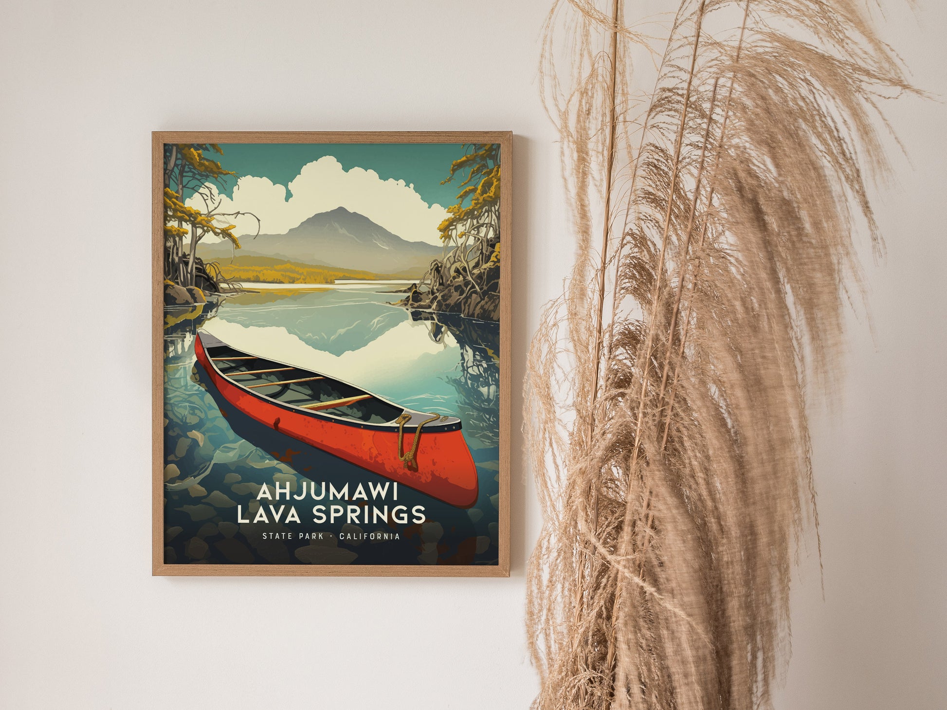 A framed poster of Ahjumawi Lava Springs features a red canoe on a reflective lake with mountains in the background. Decorative pampas grass is placed beside the artwork.
