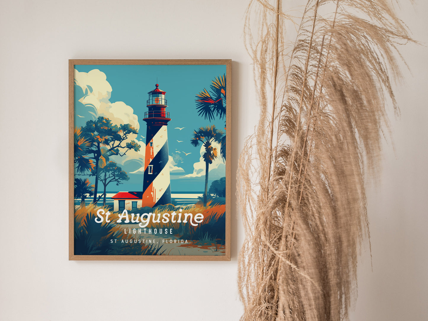 A framed poster of the St. Augustine Lighthouse, featuring a black and white spiral design, is displayed on a wall next to tall, wispy dried grass. The poster has a vintage travel art style with vibrant colors.